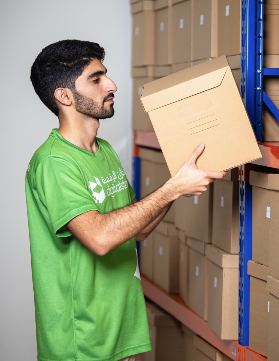 A DigitalStores associate in a branded green uniform placing a labeled box onto warehouse racking