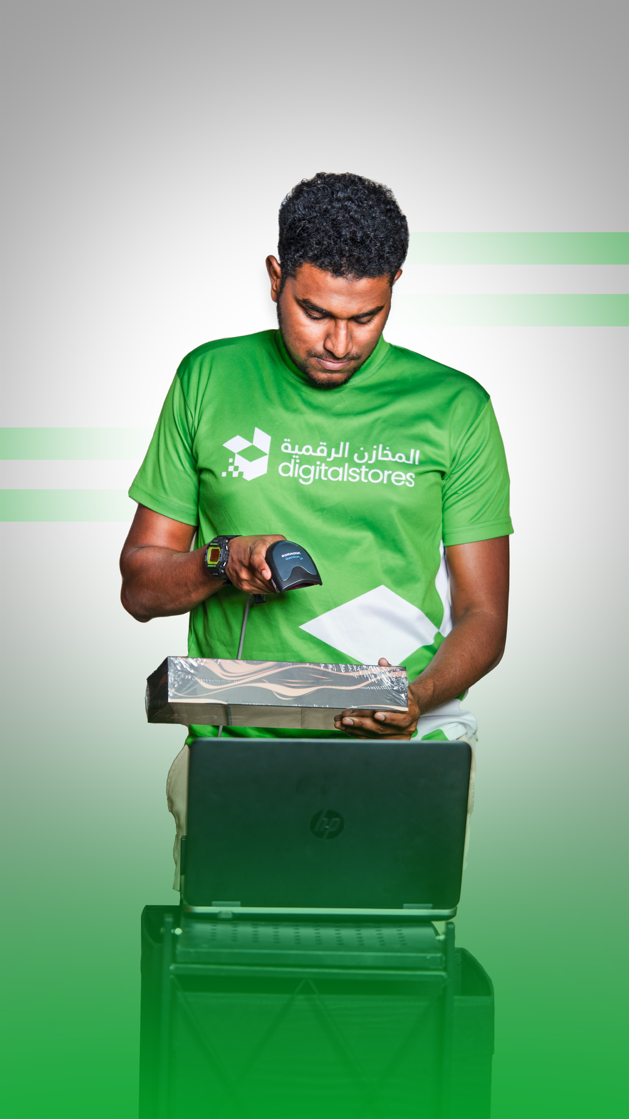 A DigitalStores associate in a branded green uniform scanning a shrink-wrapped package over a laptop at the fulfillment station